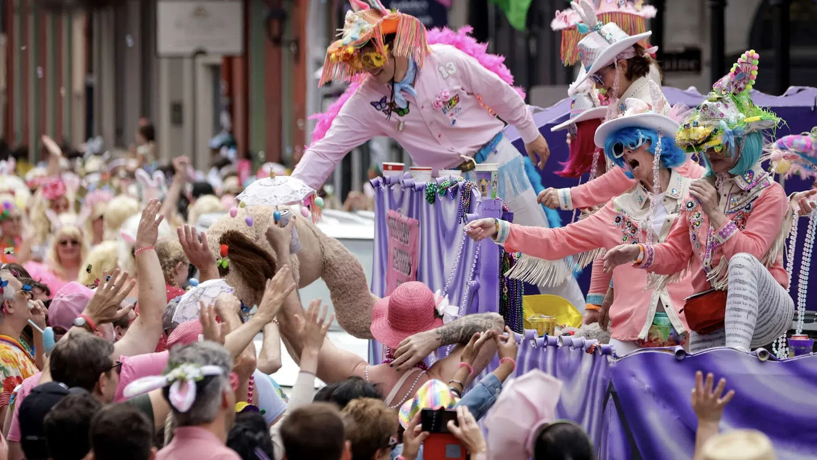 People in colorful costumes on parade float reaching out to enthusiastic crowd during festive street celebration