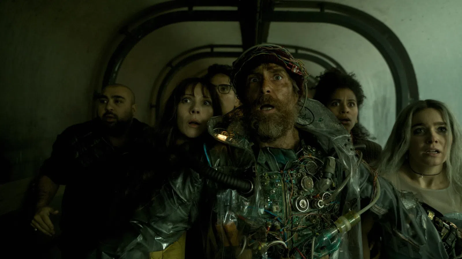 Group of six diverse people appearing frightened inside a dim, enclosed tunnel with shadows.