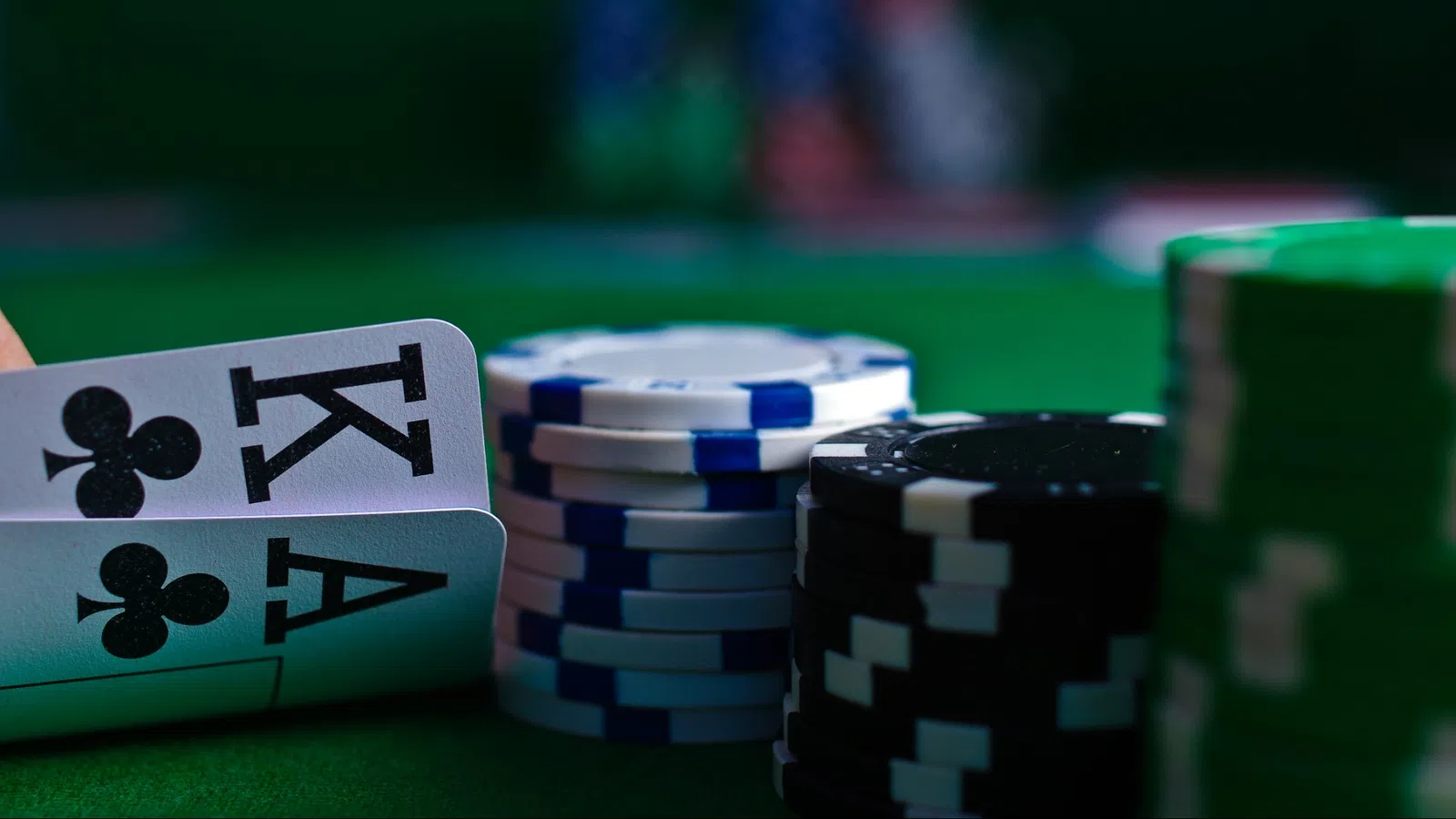 Close-up of poker table with a King and Ace of clubs and stacks of blue, black, and green poker chips.