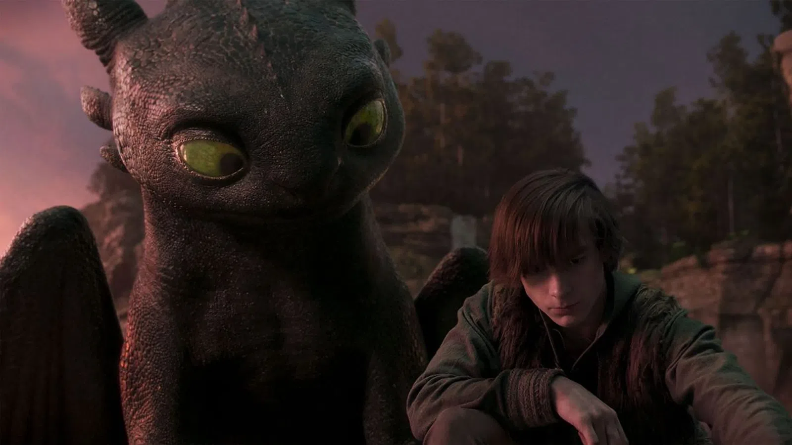Young boy sitting beside a large black dragon with green eyes during dusk in a forest setting.