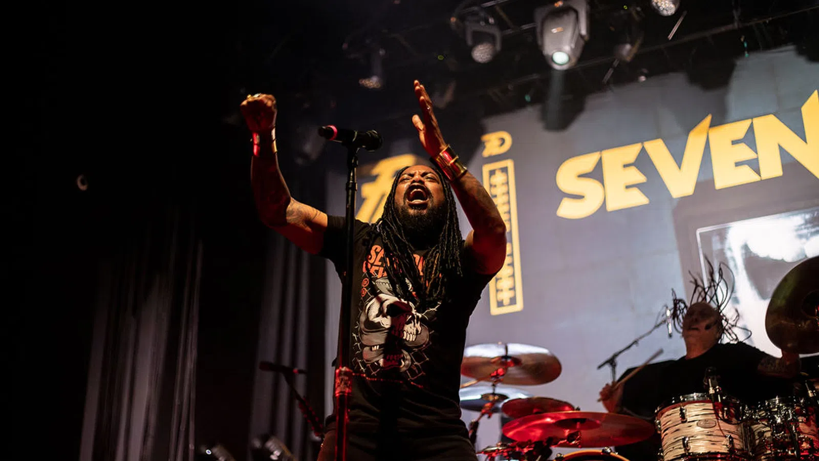 a person holding a microphone and standing in front of a drum set