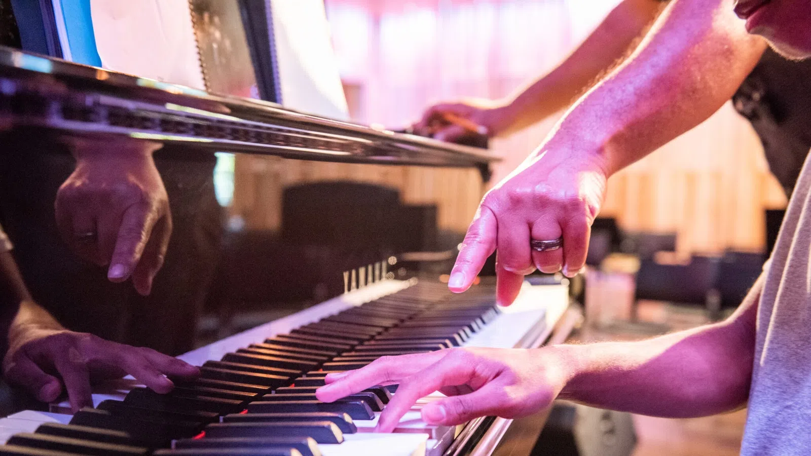 Person playing piano while another hands points at specific piano keys during a lesson.
