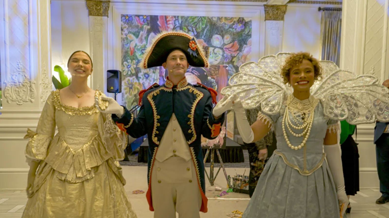 Three individuals in historical costumes pose elegantly at a vibrant event space.