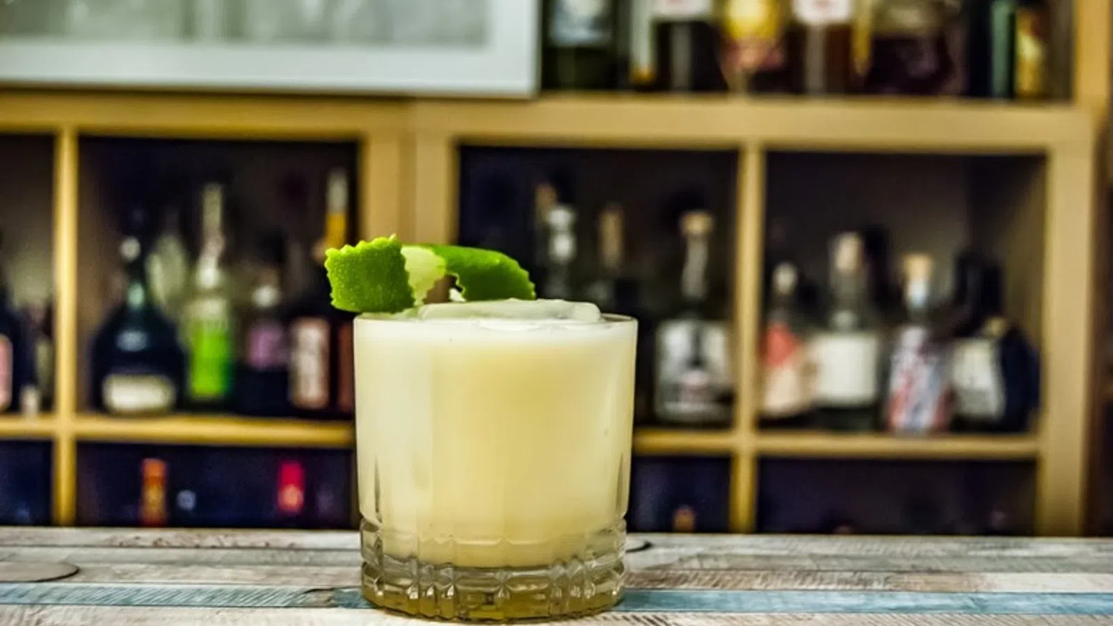 a glass of yellow liquid with a green bird on top