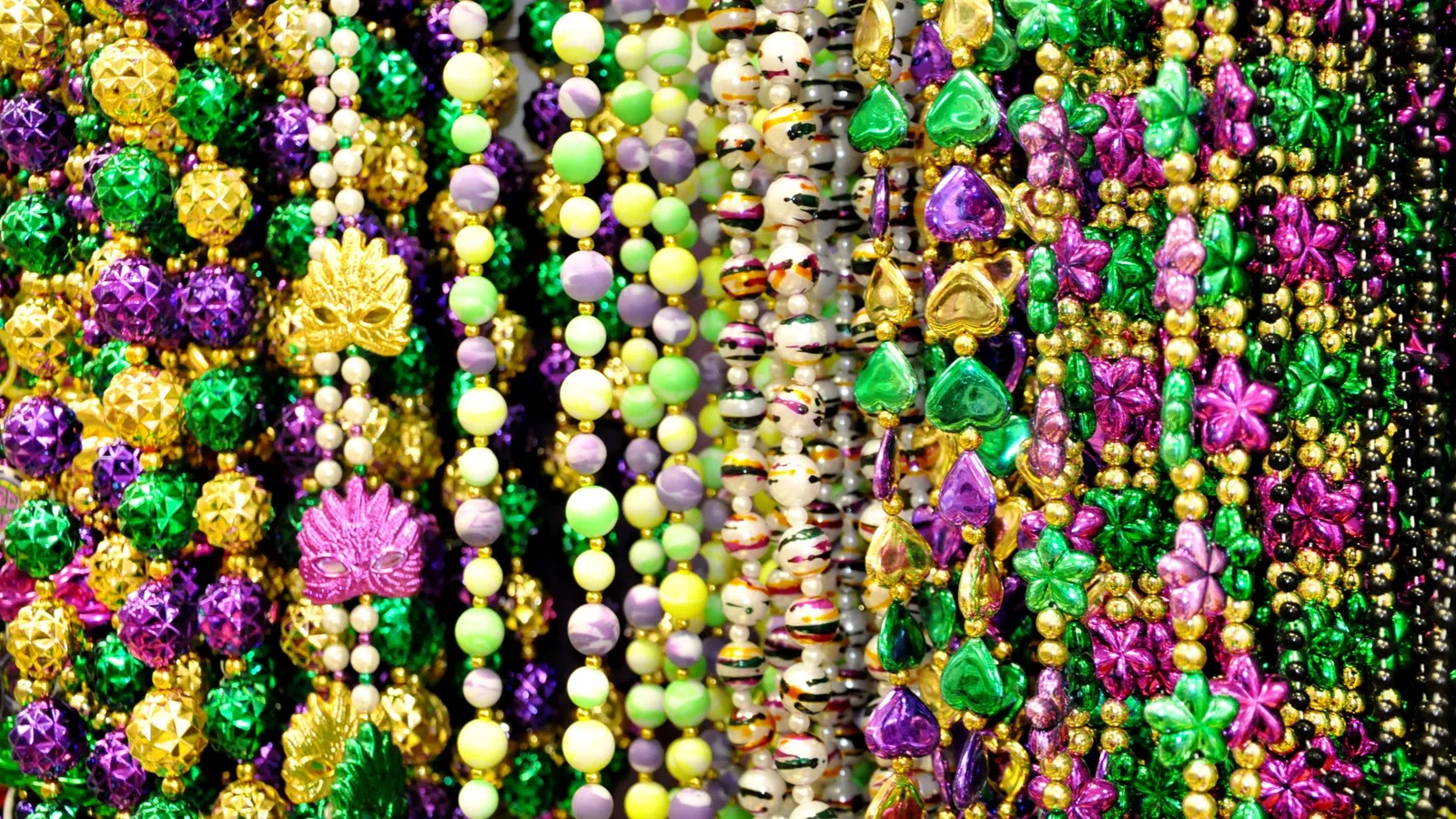 Colorful Mardi Gras beads in purple, green, gold, and yellow with various shapes and designs.
