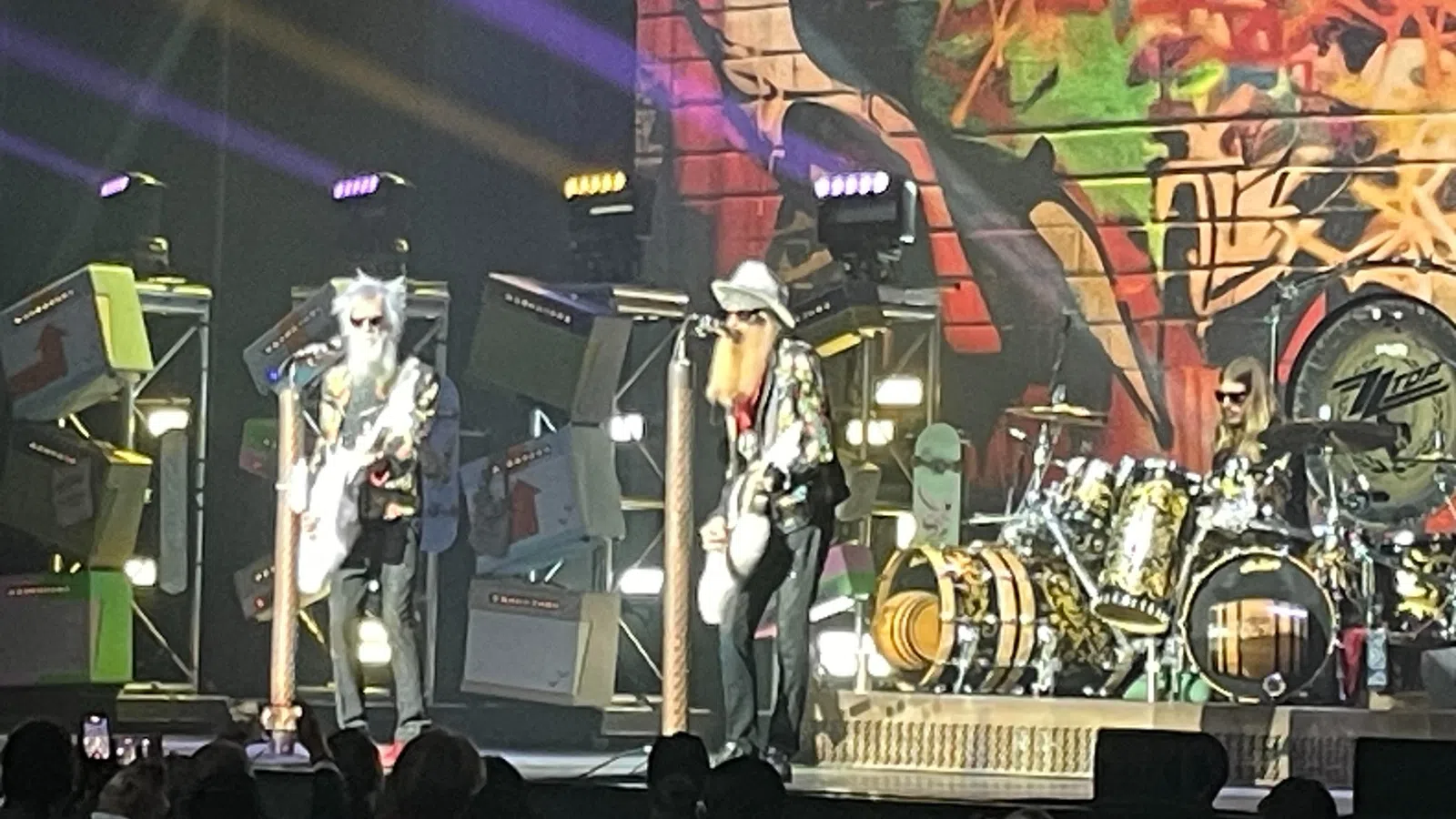 Rock band performing live on stage with colorful graffiti backdrop and bright stage lights