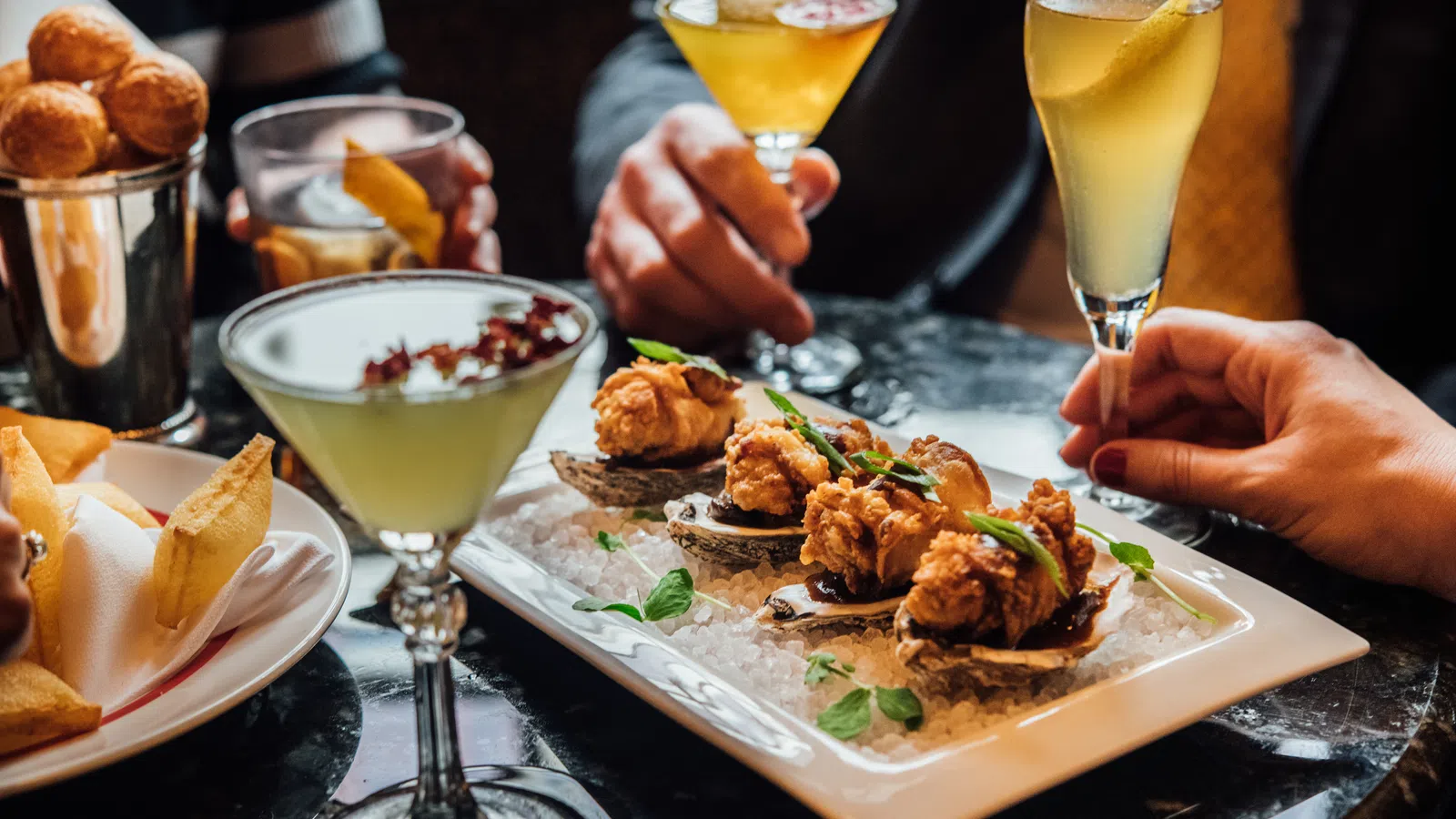 People enjoying fried oysters, cocktails, and fries on a table in a social dining setting.