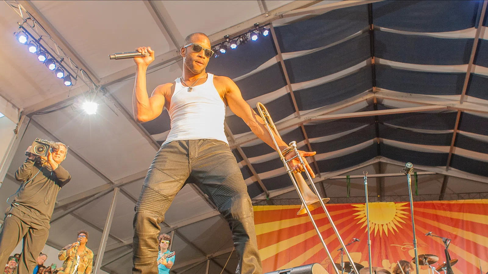 Energetic male musician on stage holding microphone and trombone under bright lights during live performance