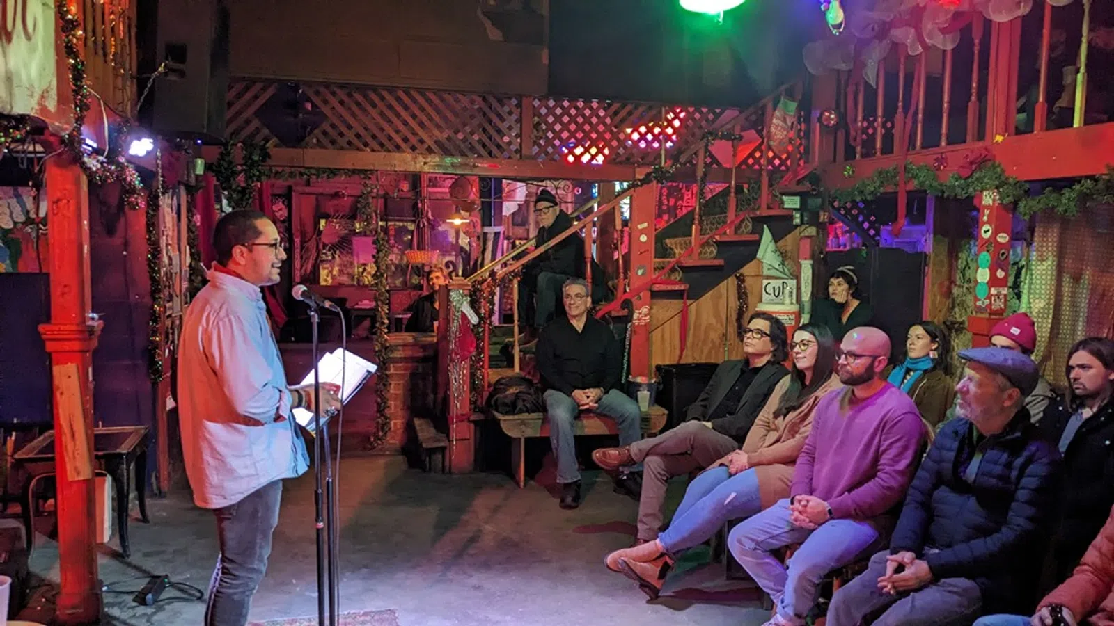 a group of people sitting in a room with a stage and a person standing in front of them
