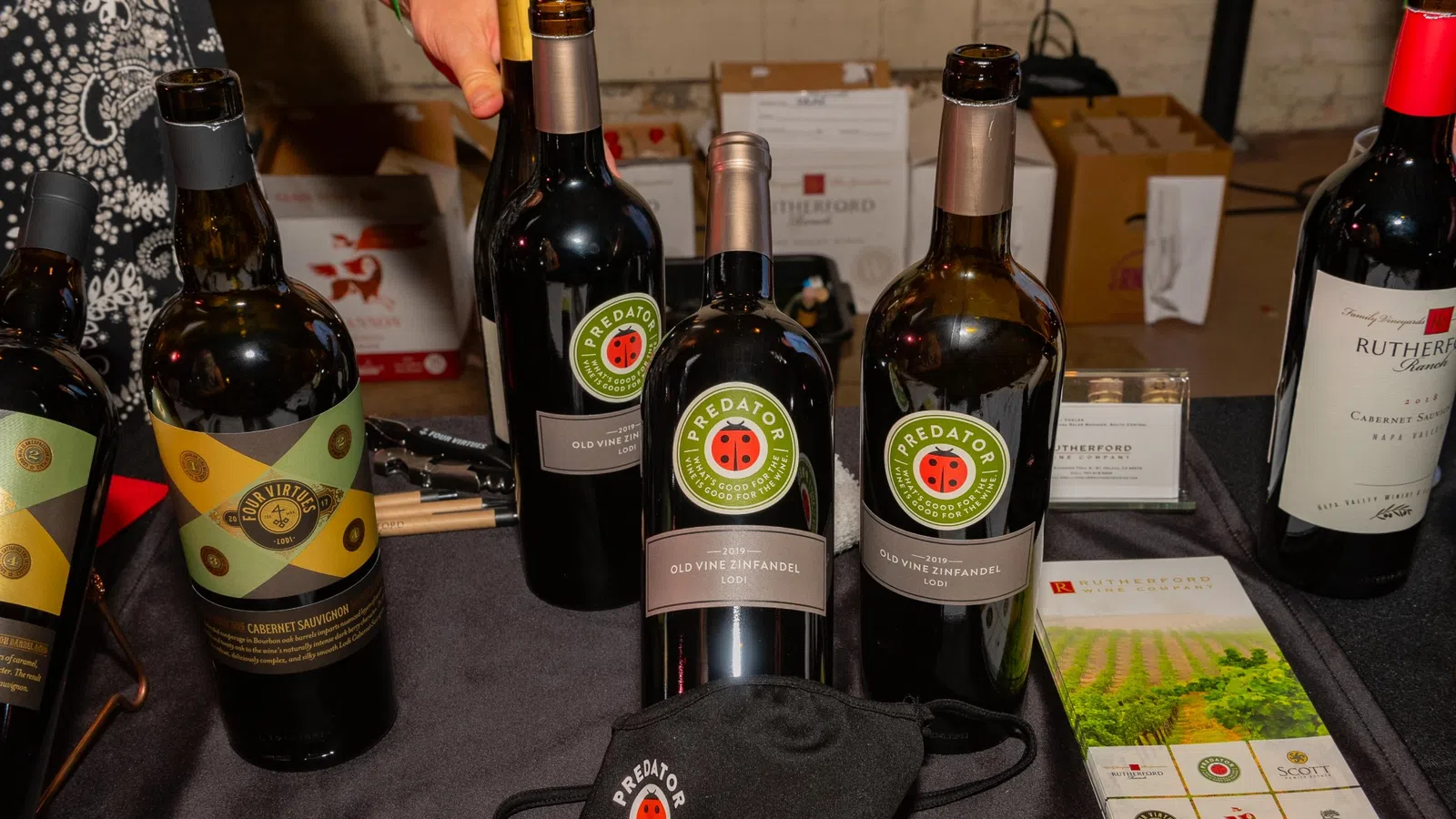 Display of multiple Predator Wines bottles, a branded mask, and promotional brochures on a table at a wine event.