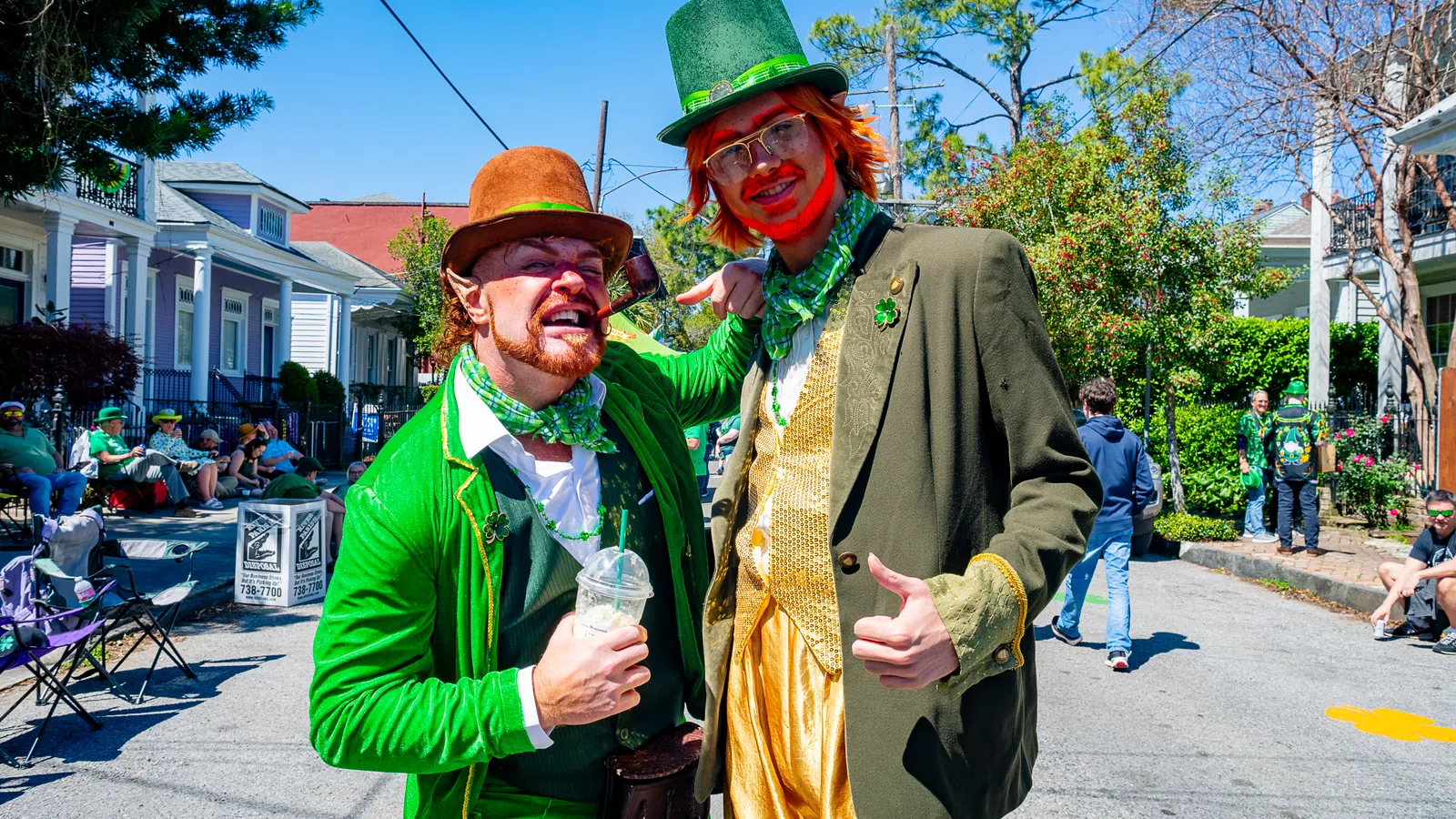 Two men dressed as festive leprechauns in green and gold costumes during a street celebration
