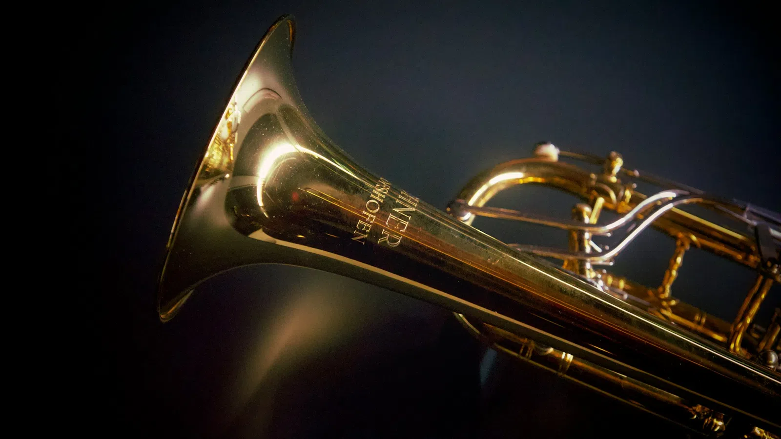 Close-up of golden brass trumpet with visible valves against a dark background and soft lighting highlights.