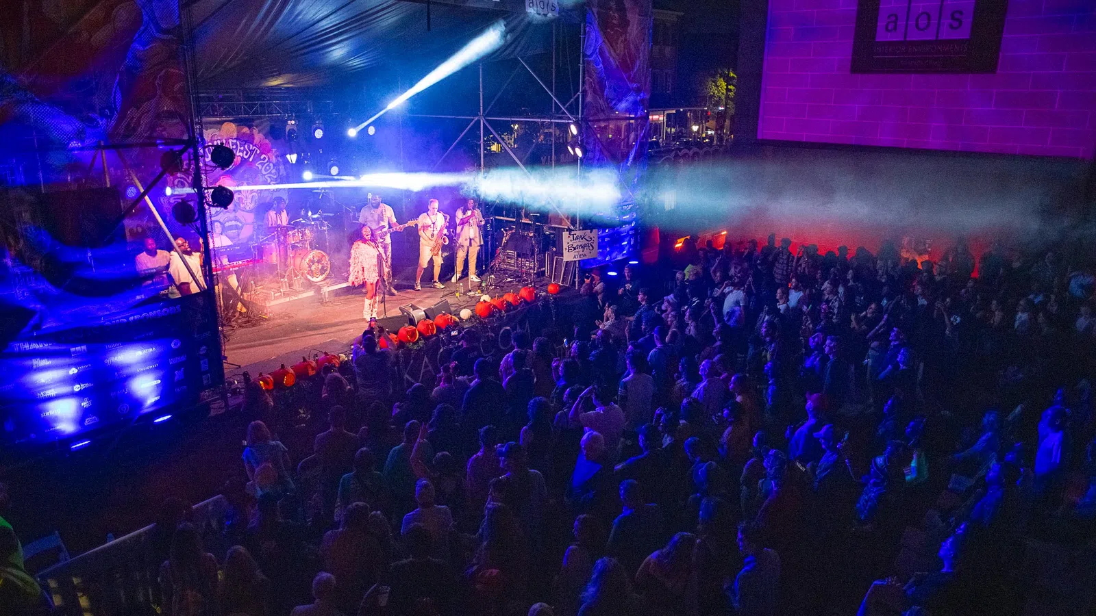 Live band performing on AOS Main Stage with colorful lights and large crowd at night concert event.