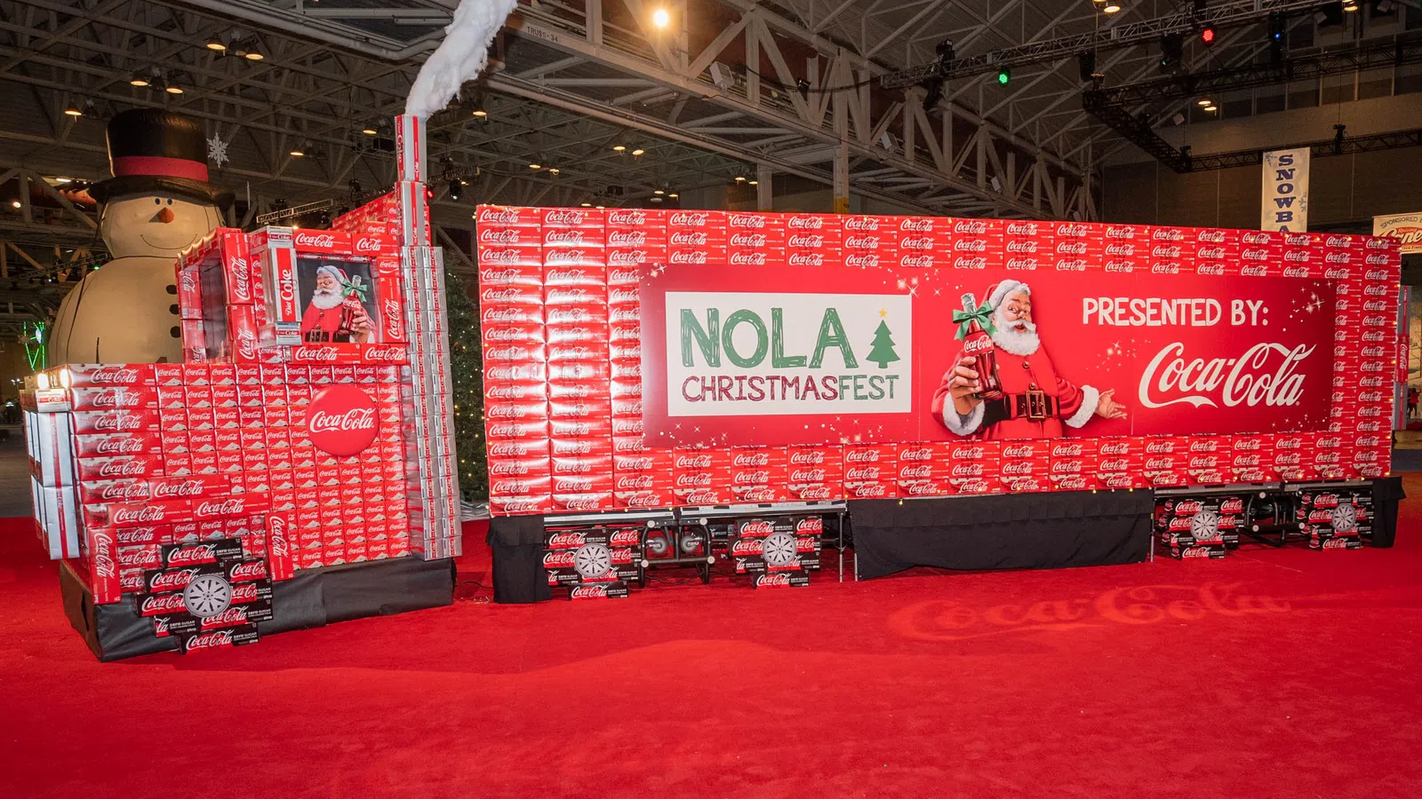 NOLA ChristmasFest display built from Coca-Cola boxes with Santa and snowman decorations indoors.