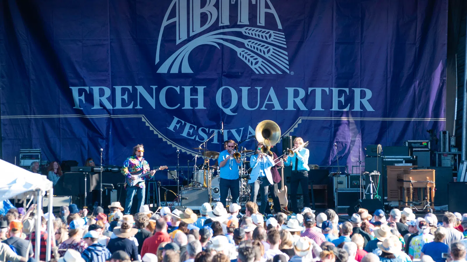 Live band performing on stage at Abita French Quarter Festival with large crowd wearing hats and colorful outfits