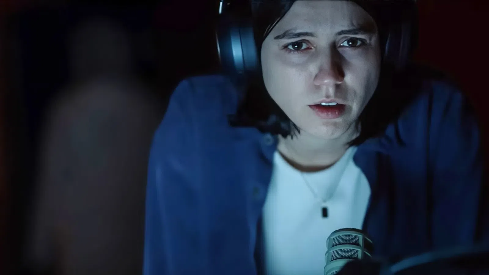Close-up of a serious young woman wearing headphones speaking into a microphone in a dark room.