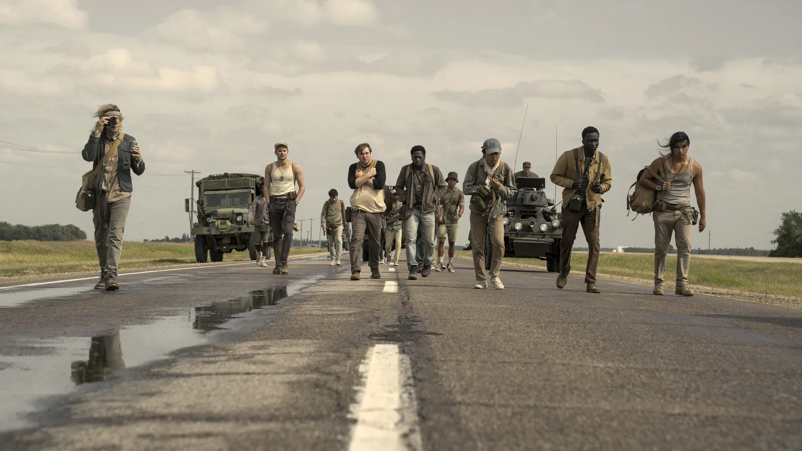 Group of diverse people walking on a rural road with military vehicles under cloudy skies