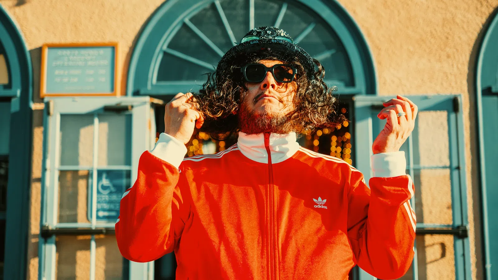a man wearing sunglasses and a red jacket with his hands up