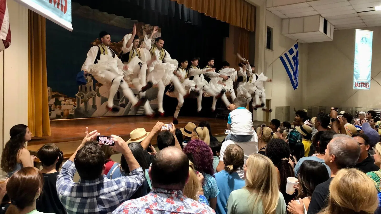Traditional Greek dancers performing on stage in front of a large audience capturing the lively cultural event.
