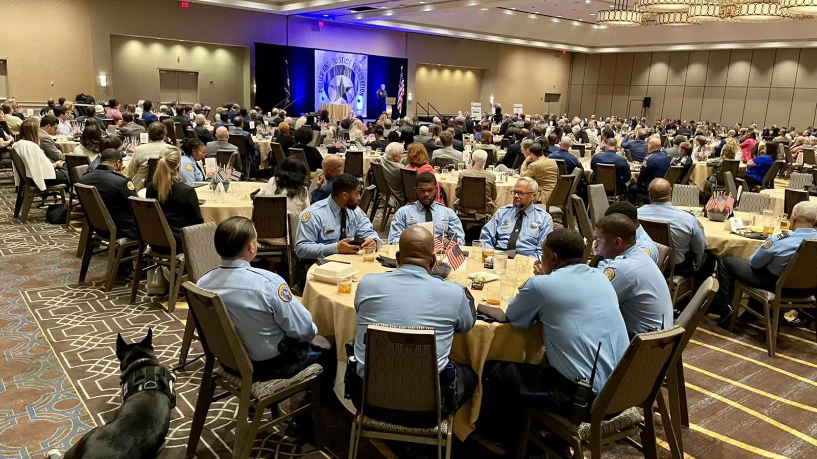 Law enforcement officers in uniform seated at round banquet tables during a formal indoor conference or ceremony.