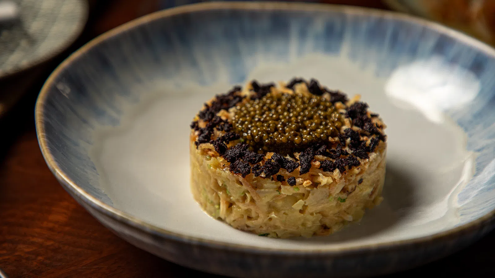 Gourmet dish with finely chopped ingredients topped with black and golden caviar on a ceramic plate.