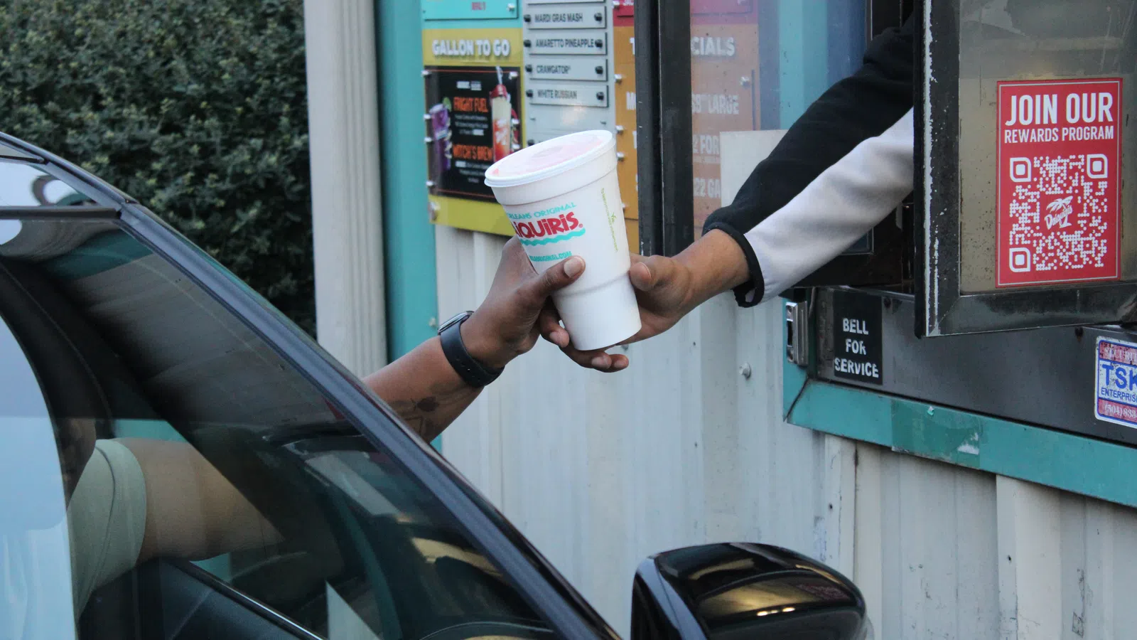 Drive-thru service handing a large White Castle drink cup to a customer in a black car at the ordering window
