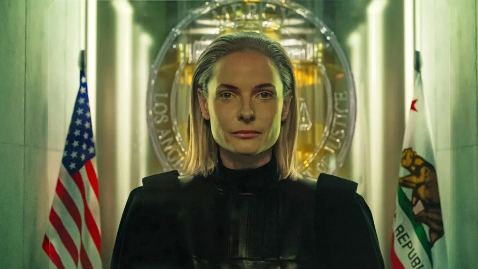 Serious woman in black attire standing between American and Californian flags with official seal in background