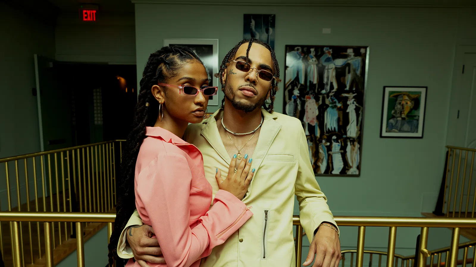 Stylish couple posing in trendy outfits indoors with art in the background.