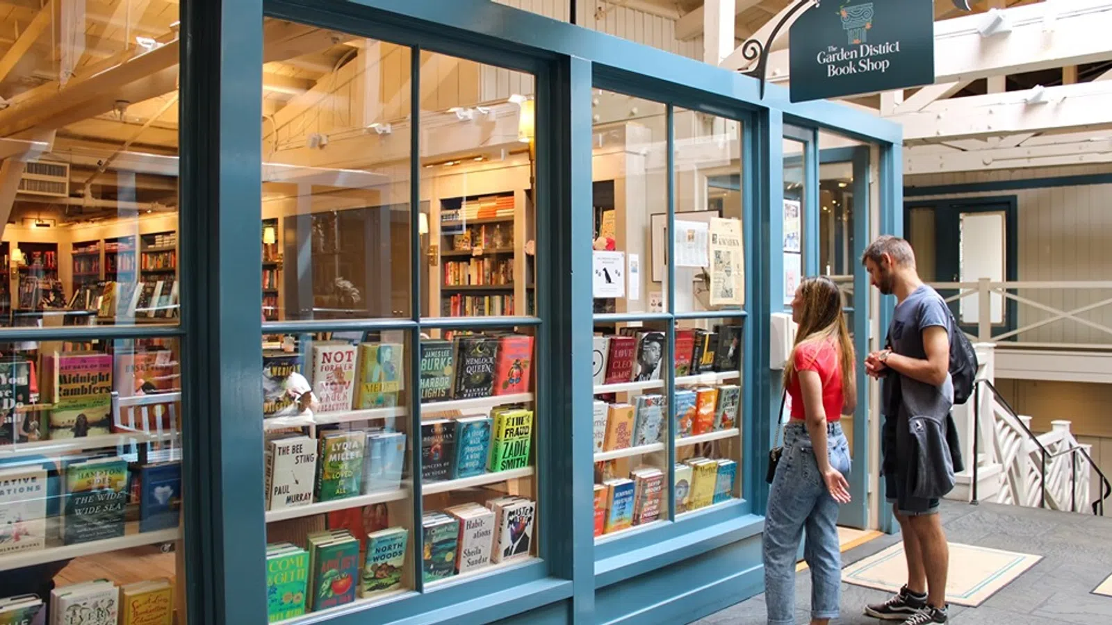 Couple browsing books displayed in the window of a cozy independent bookstore with blue framing inside a wooden building