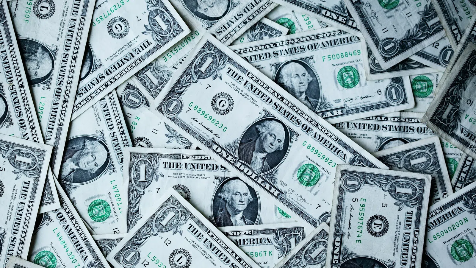 Multiple one dollar US banknotes scattered, showing George Washington's portrait and currency details.