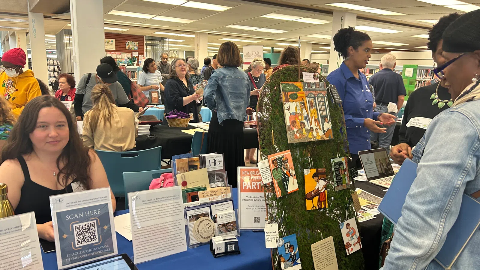People explore informational booths at a busy community event in a well-lit indoor space with displays and artwork.