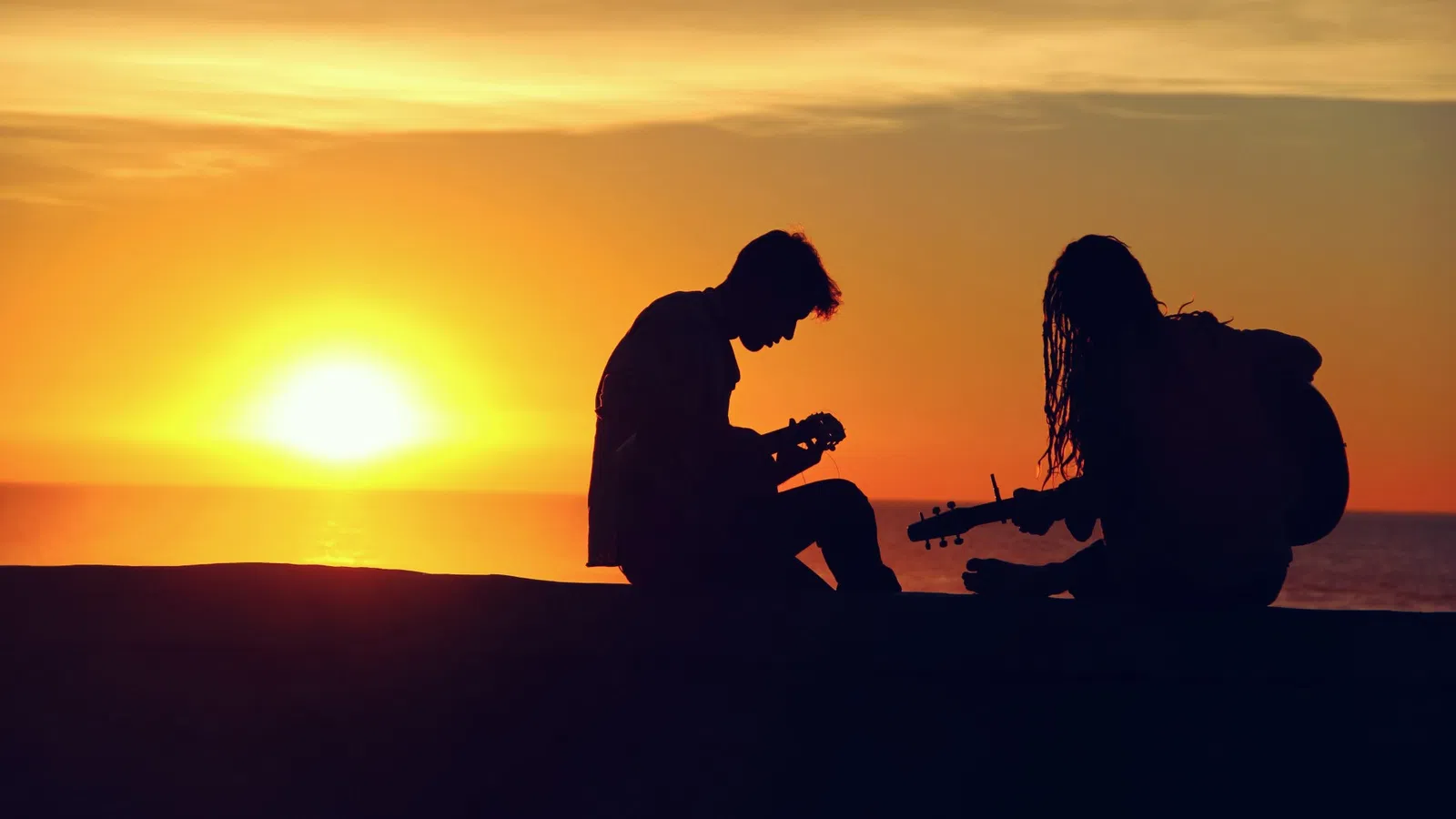 a man and woman sitting on a rock with the sun setting behind them