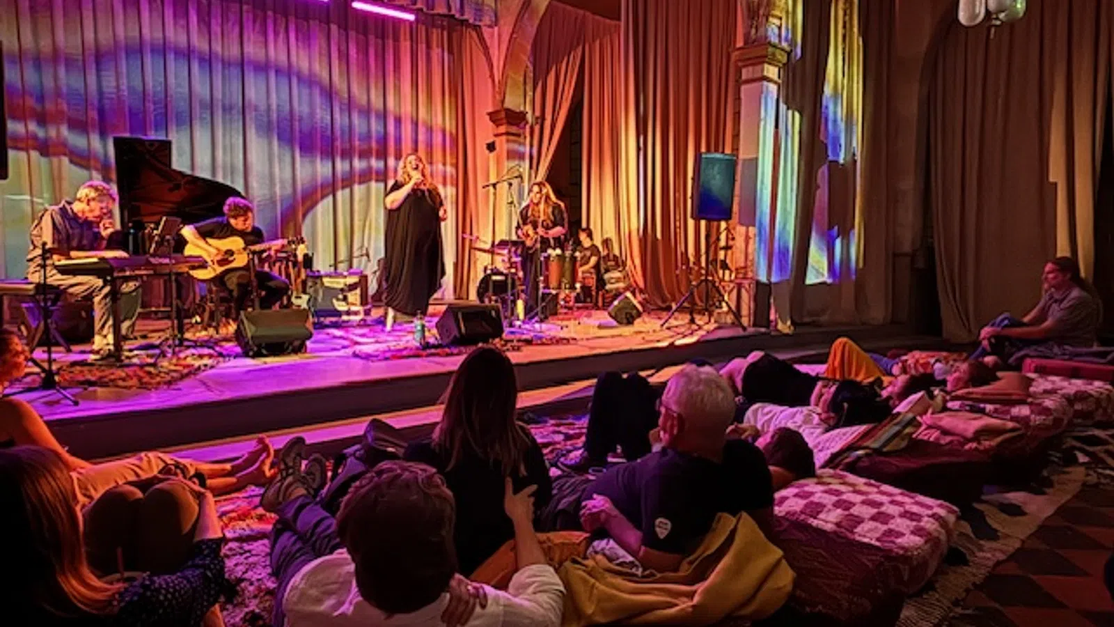 Intimate live music performance with colorful lighting and a cozy audience setting.