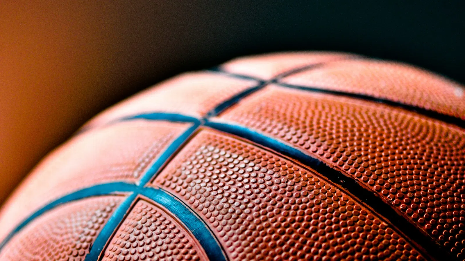 Close-up of an orange basketball showing textured surface and black lines against a blurred background