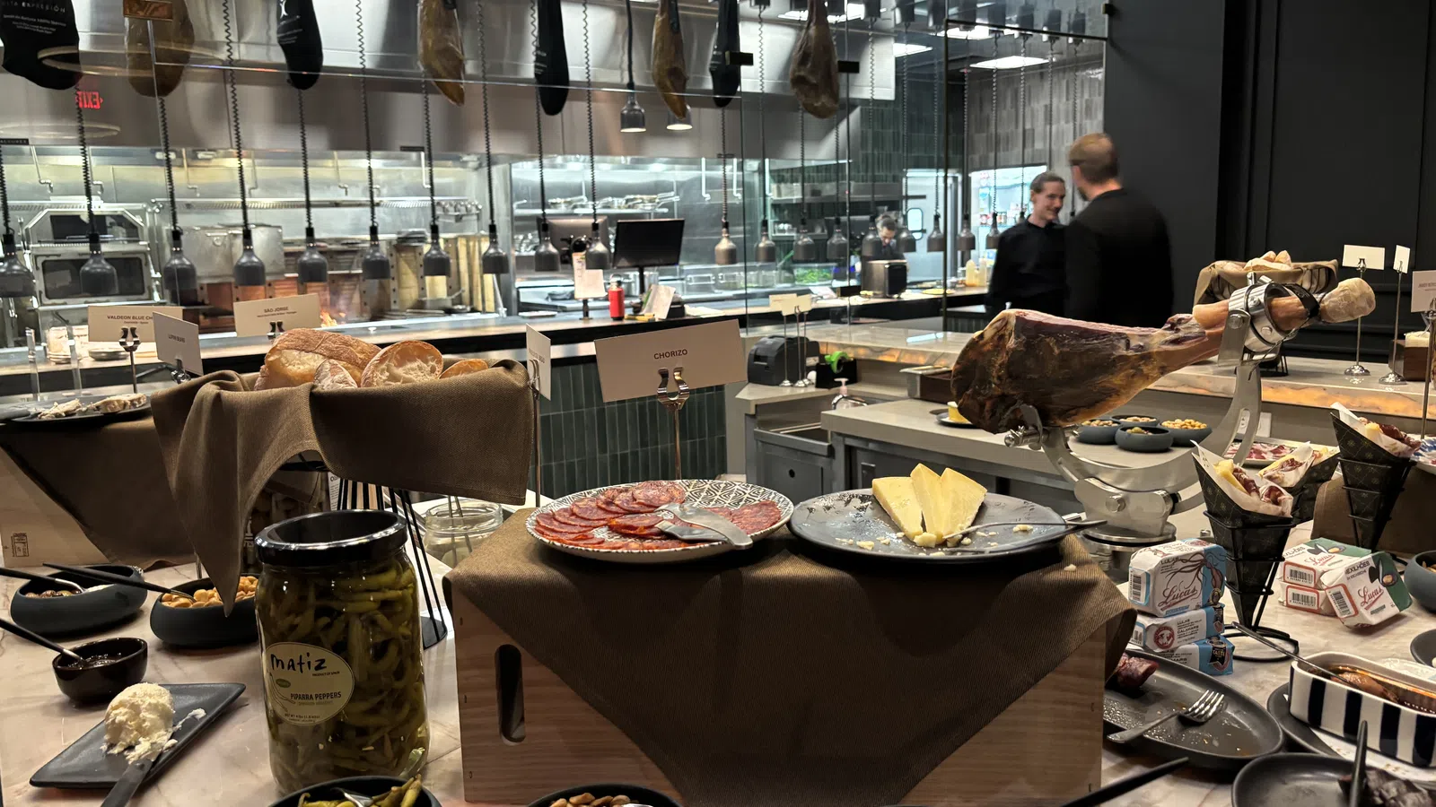 Charcuterie spread with cured meats, cheeses, nuts, pickles, and bread in a modern kitchen setting.