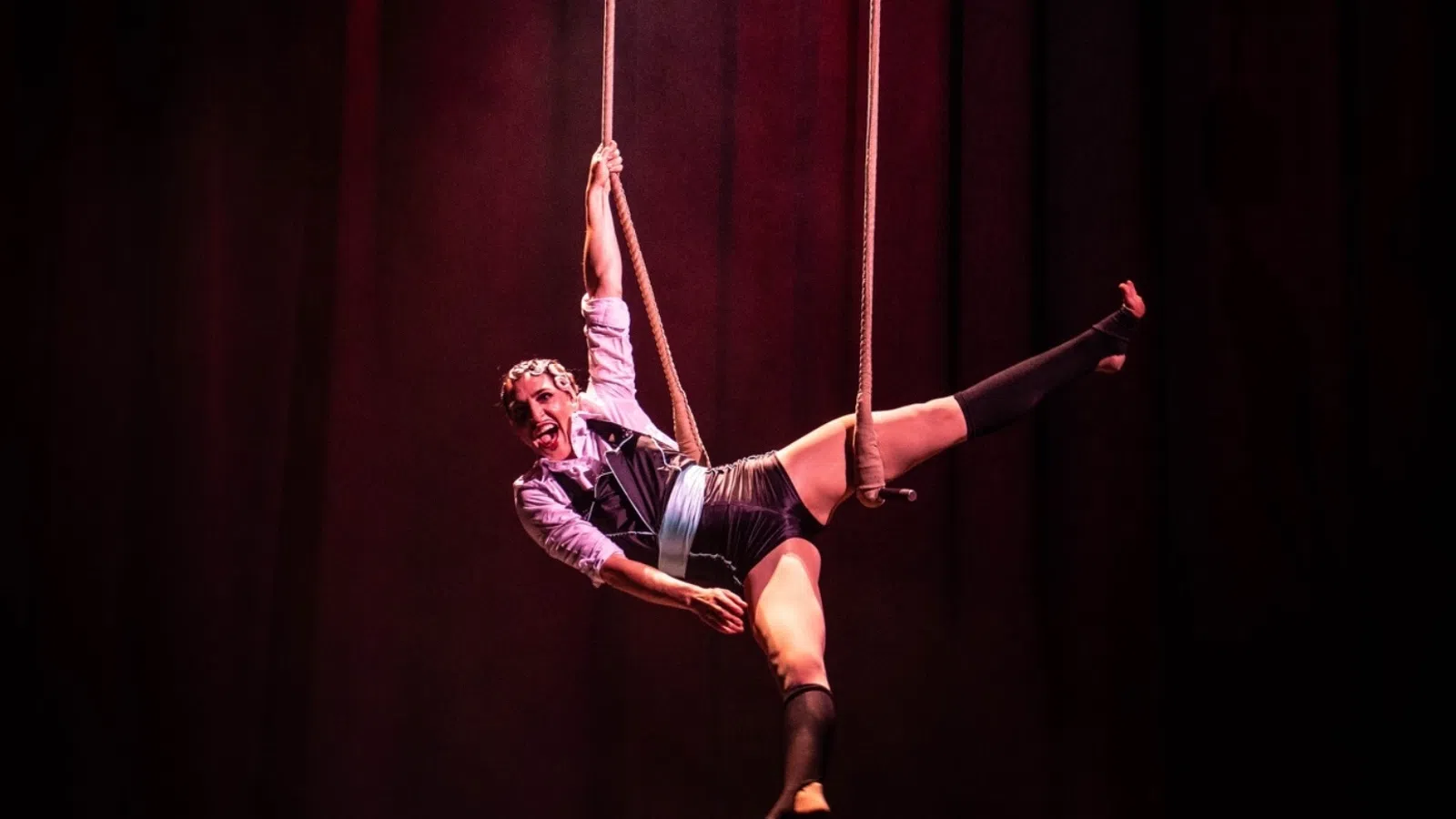 Two acrobats performing aerial stunts on ropes, with dramatic lighting and a vibrant stage backdrop.