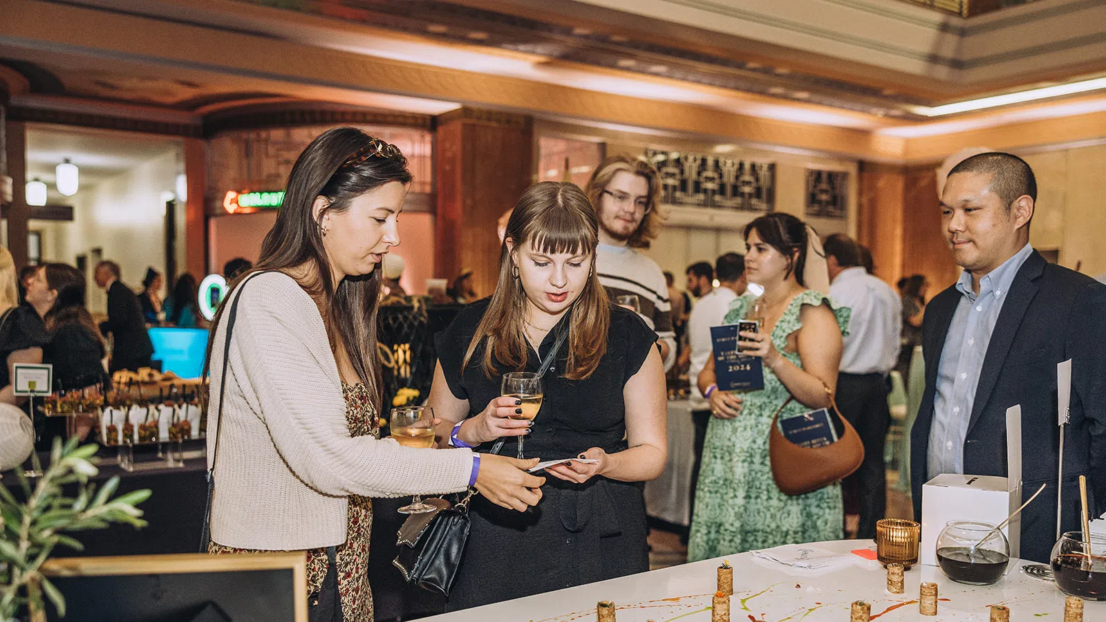 People dressed in semi-formal attire sampling wine and engaging at a social tasting event indoors.