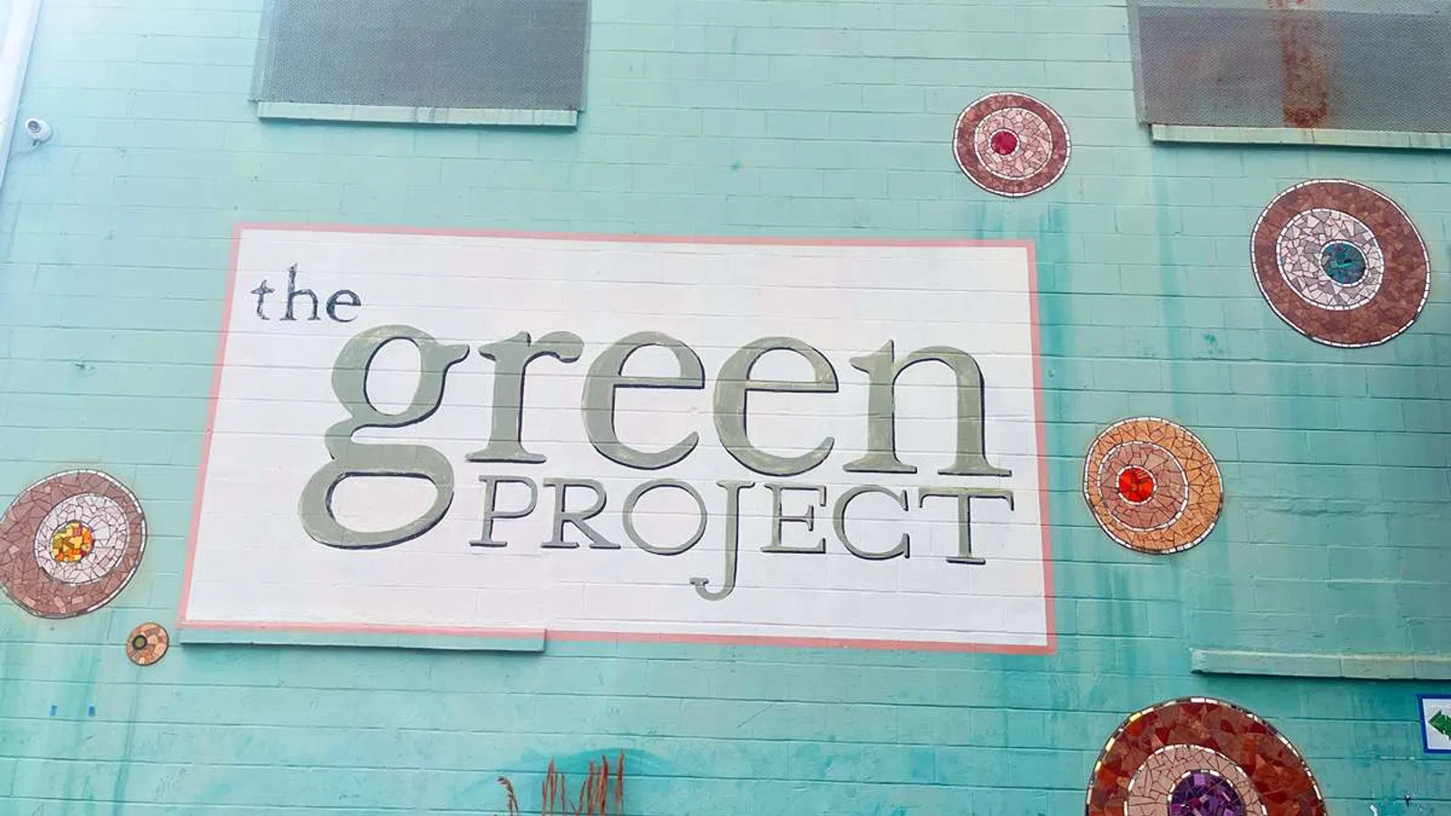 Mural on turquoise wall reading The Green Project with decorative circular mosaic art around it.