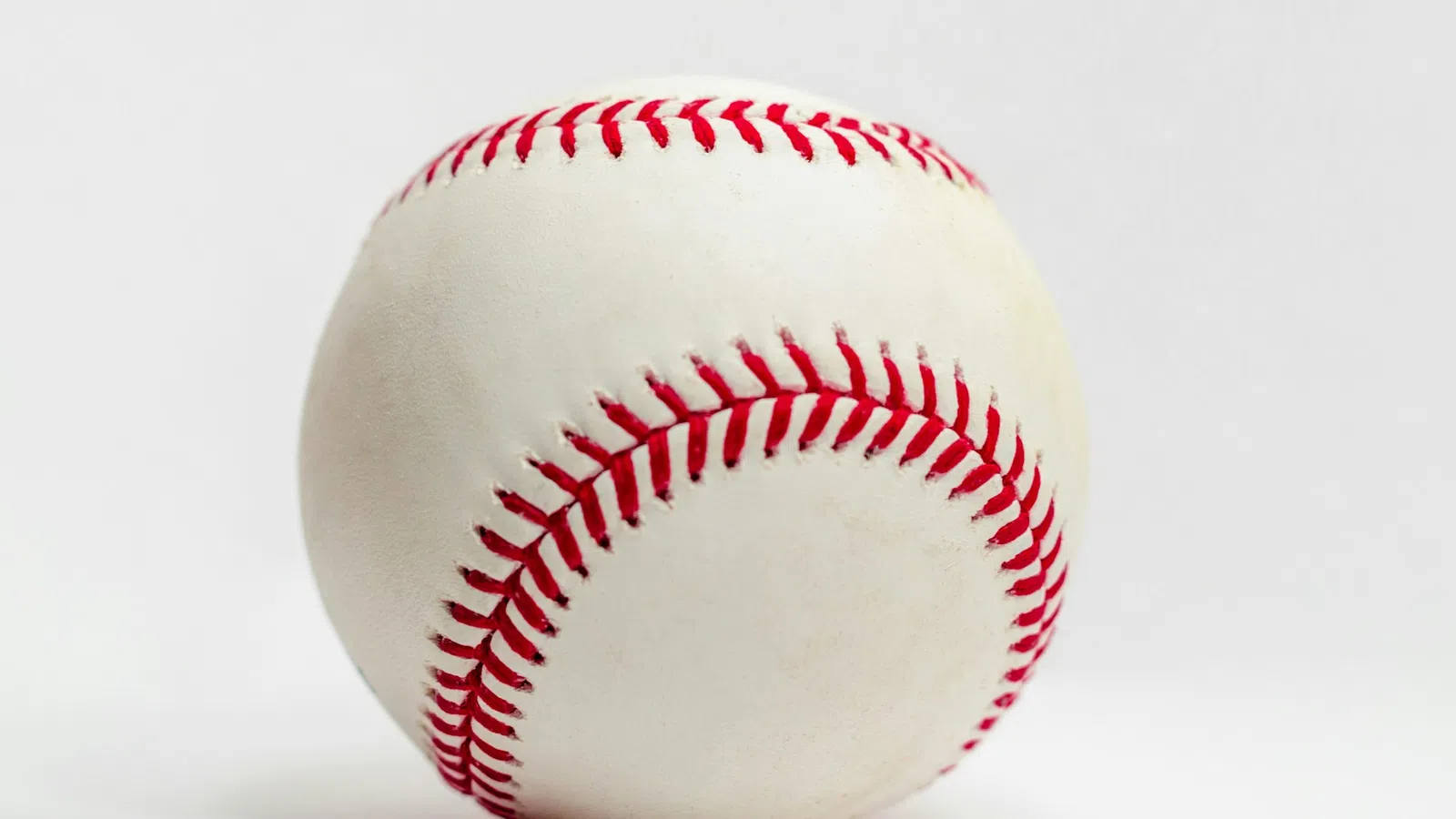 Close-up of a white baseball with red stitching on a plain white background