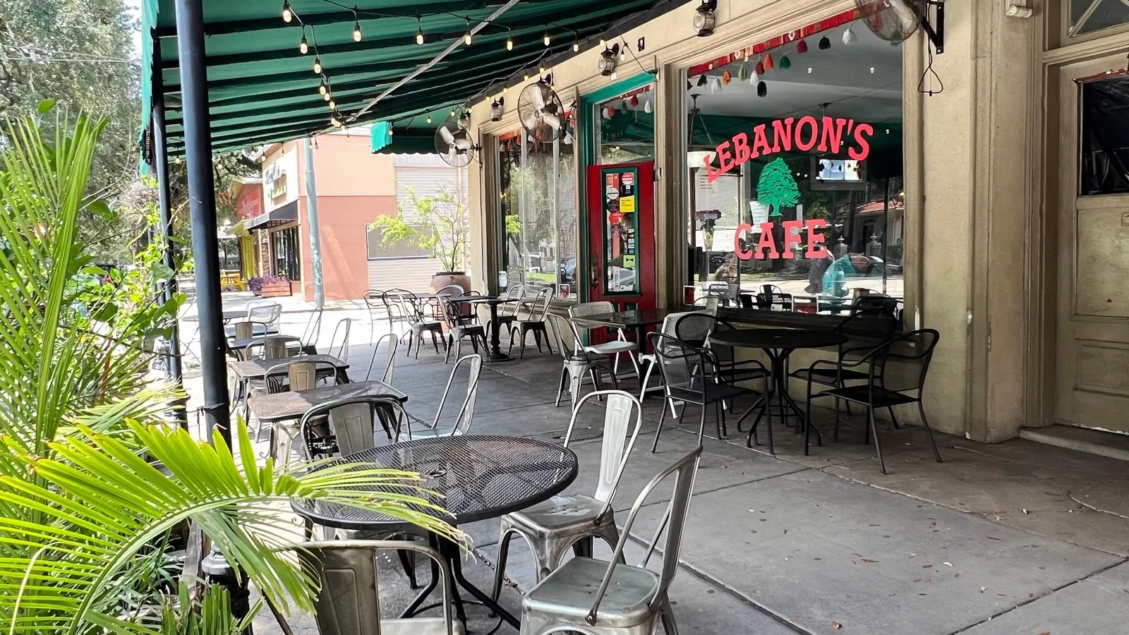 Outdoor seating area at Lebanon's Cafe with metal tables and chairs under green awning on sunny day