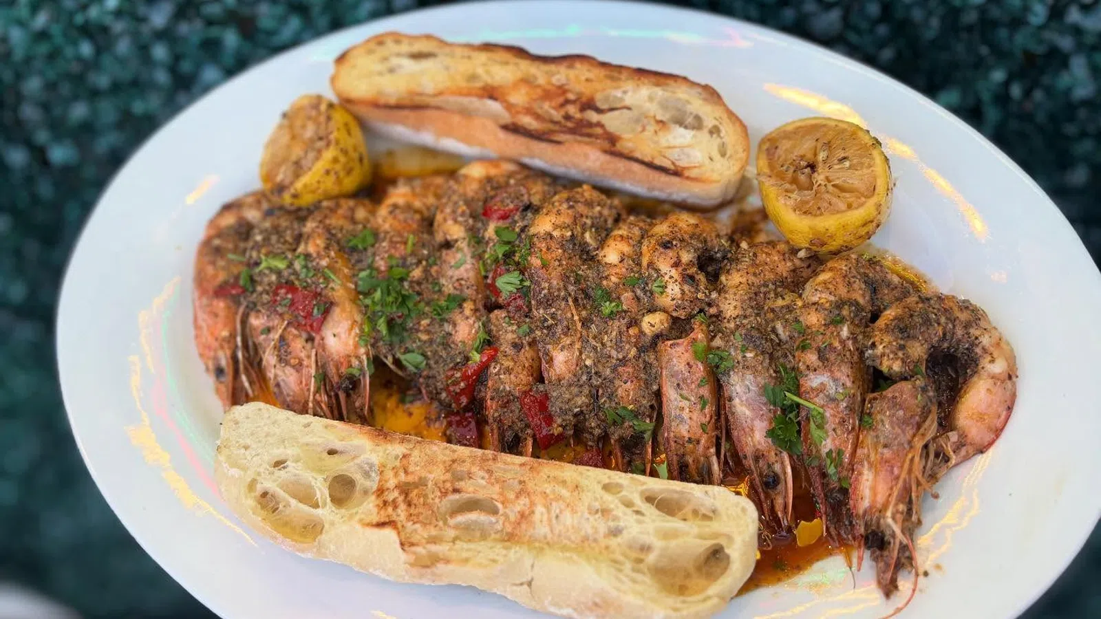 Grilled seasoned shrimp served with toasted bread and lemon halves on a white plate.