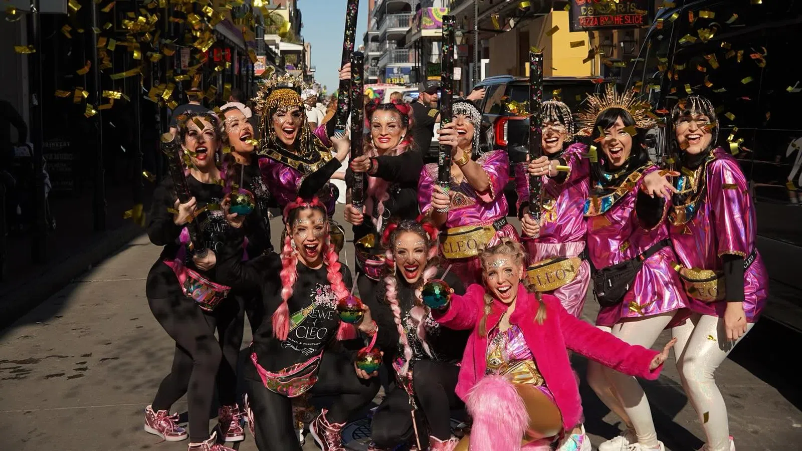 Group of women in colorful costumes celebrating on a city street with confetti and smiles during daytime event