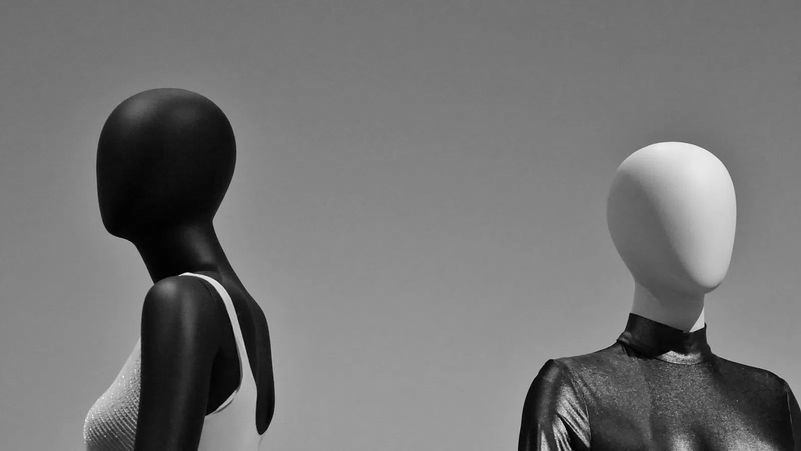 Black and white mannequins wearing contrasting white and black outfits against a gray background.