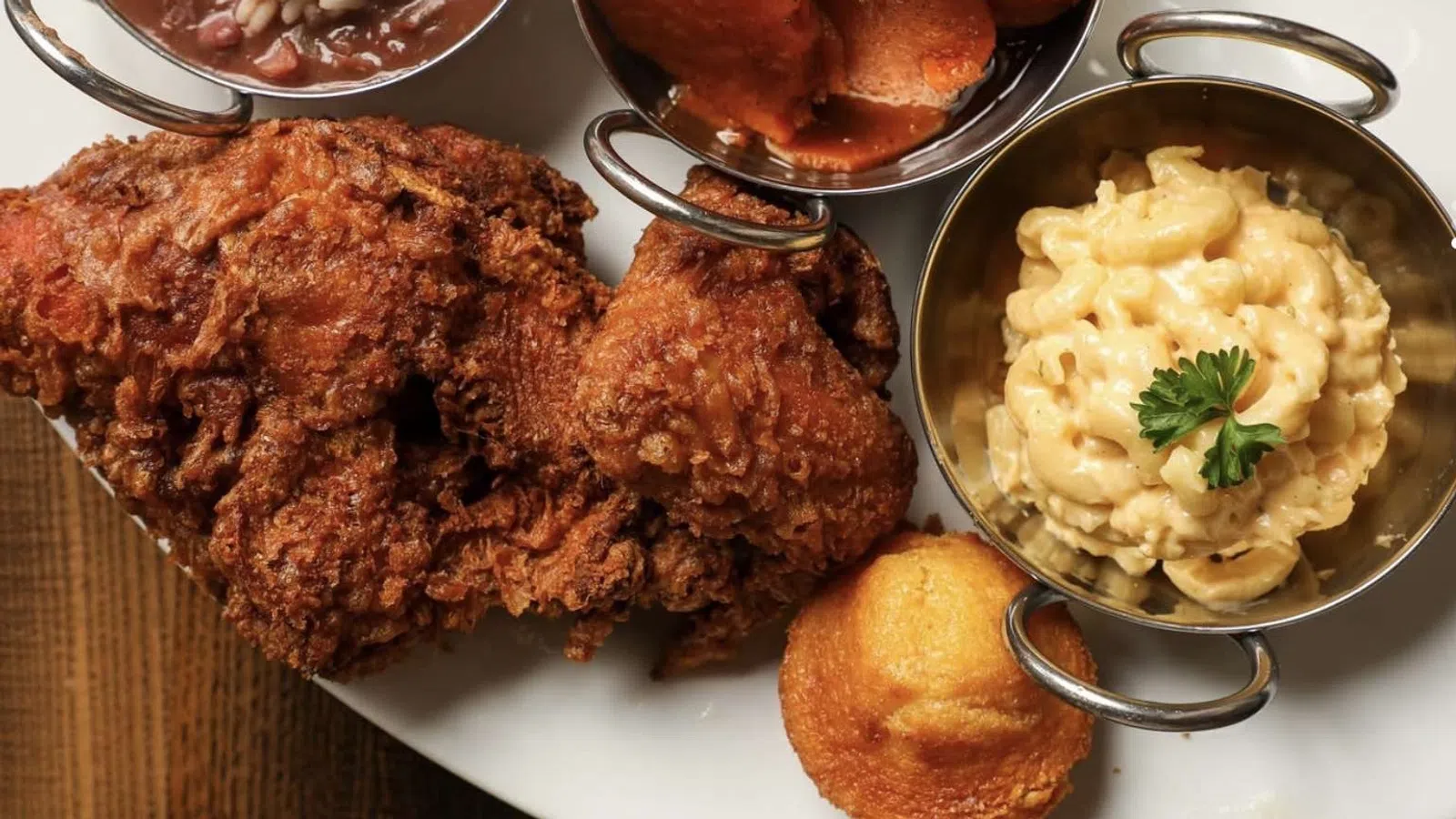 Plate with crispy fried chicken, cornbread muffin, mac and cheese, candied yams, and red beans with rice.