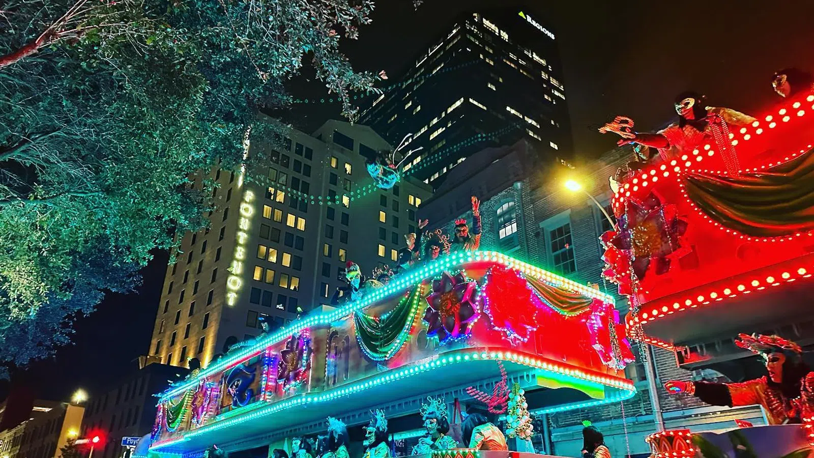 Colorful Mardi Gras parade floats with people in costumes celebrating at night in a city street.