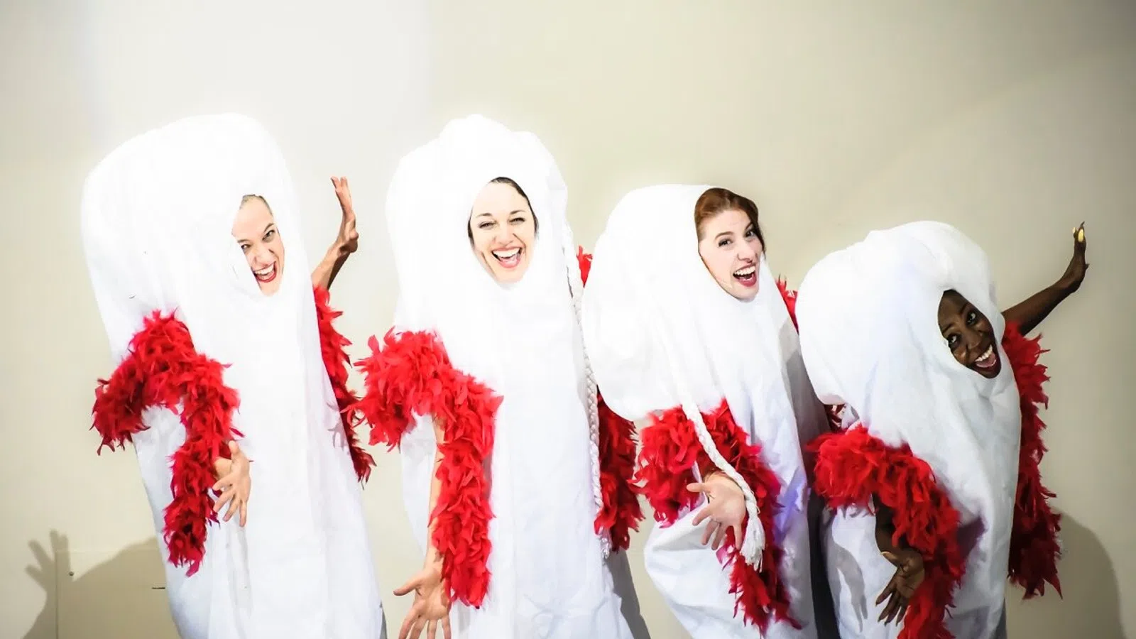 Group of four performers in creative white and red costumes, joyfully posing together on stage.