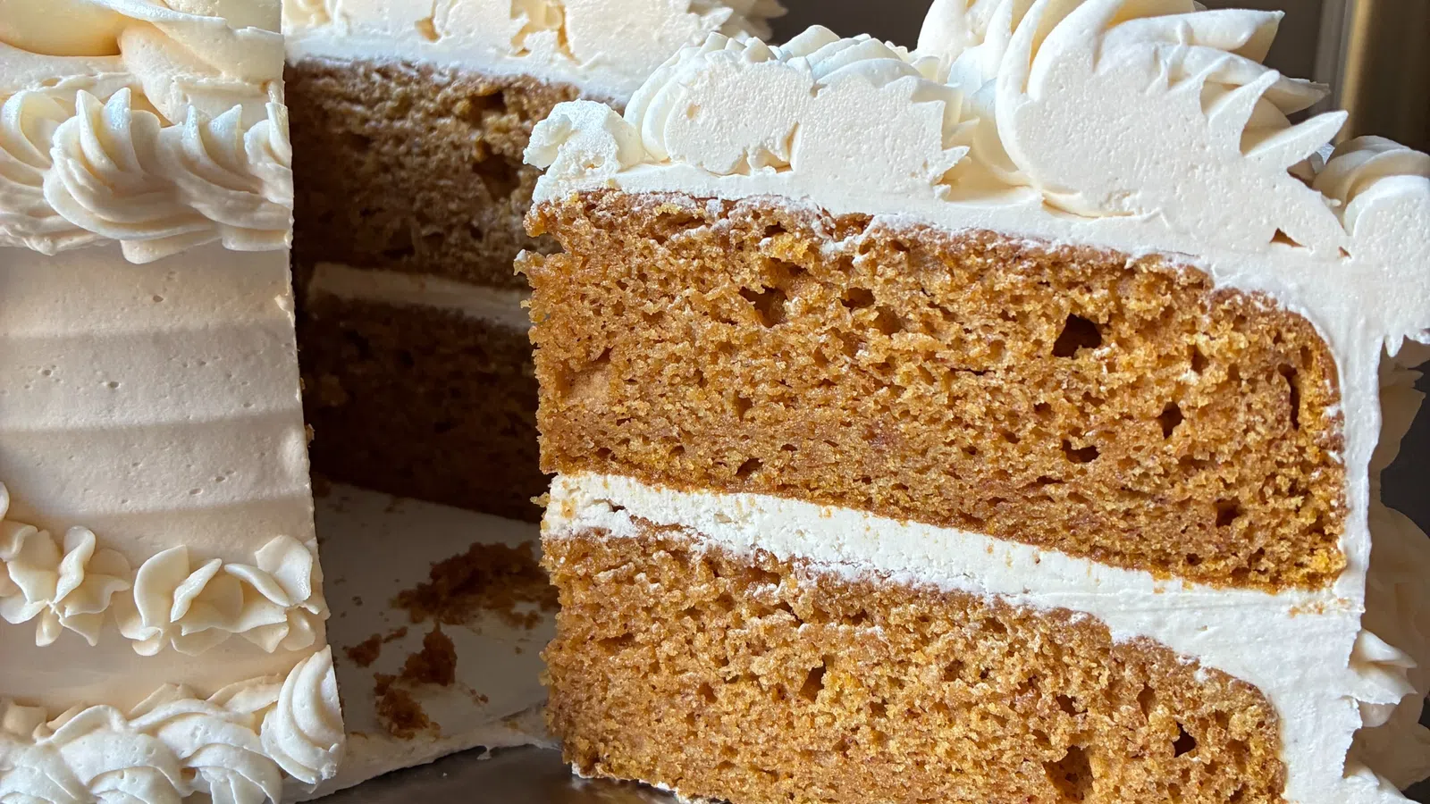 Close-up of a sliced two-layer brown cake with white frosting and decorative icing on top and sides.