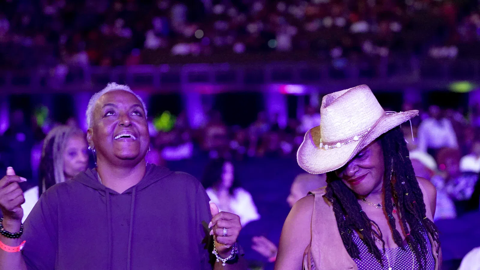 Two women enjoying music, one smiling with eyes closed wearing a cowboy hat, the other with short hair and a hoodie.