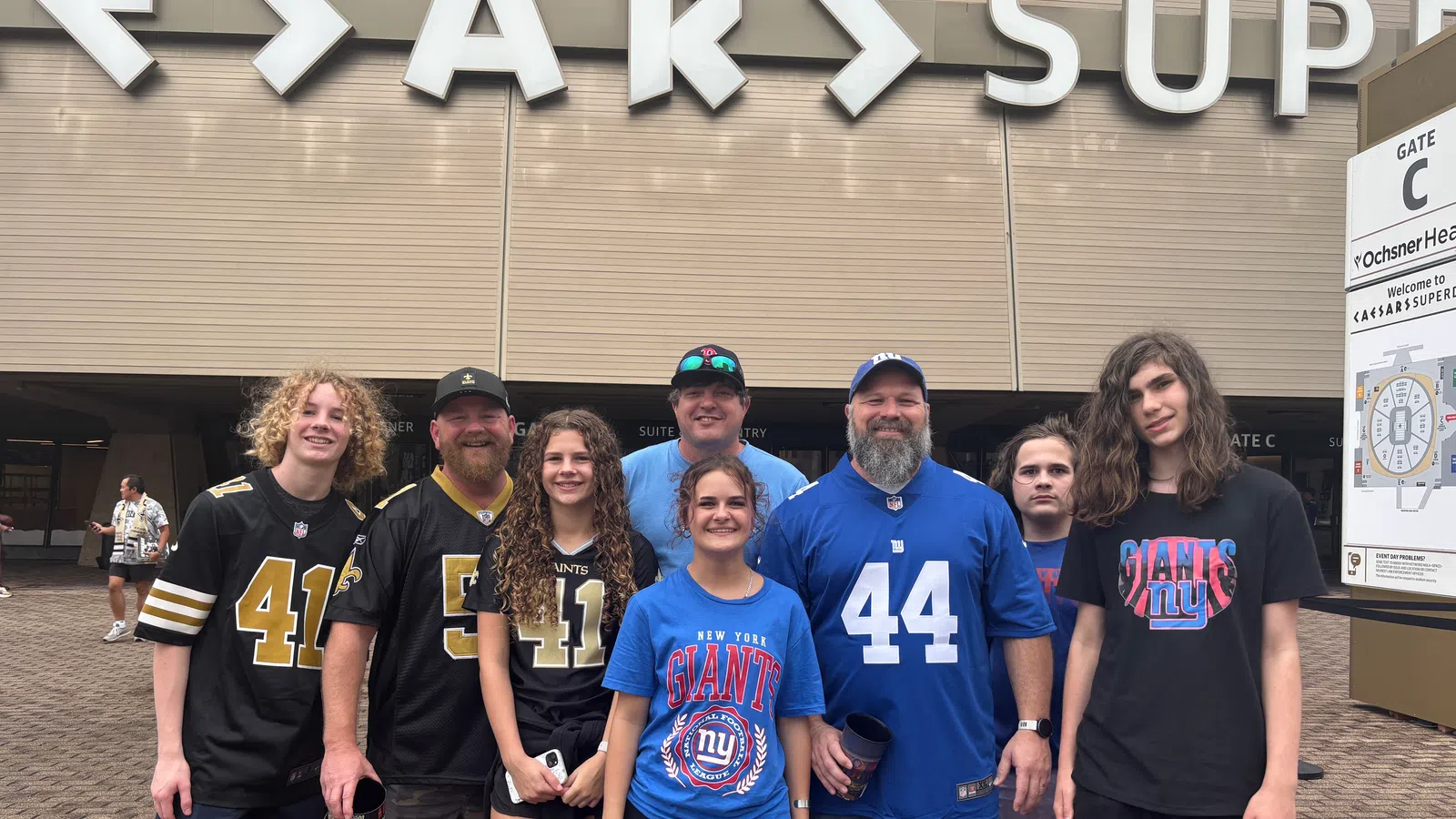 Group of New Orleans Saints and New York Giants fans posing outside Caesars Superdome stadium entrance.