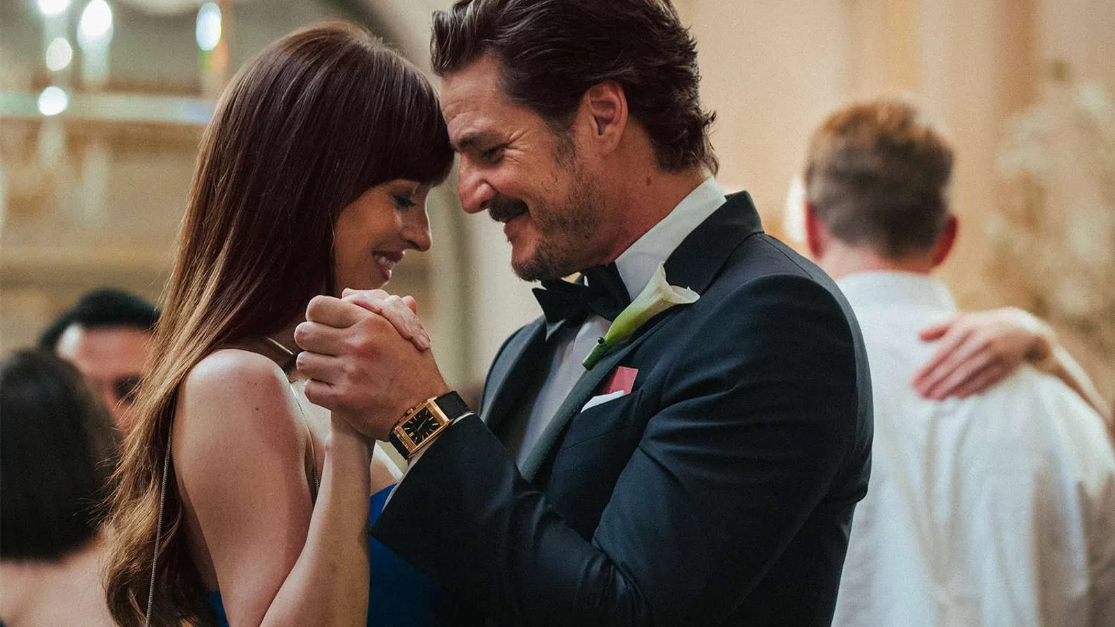 Couple in formal attire dancing closely and smiling at a romantic indoor event with other guests in background